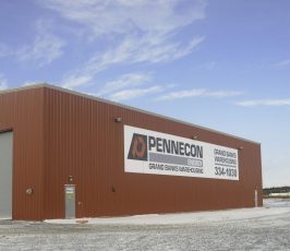 A large red metal warehouse with a sign reading "PENNECON GRAND GANG WAREHOUSE" stands in a snowy lot under a partly cloudy sky.