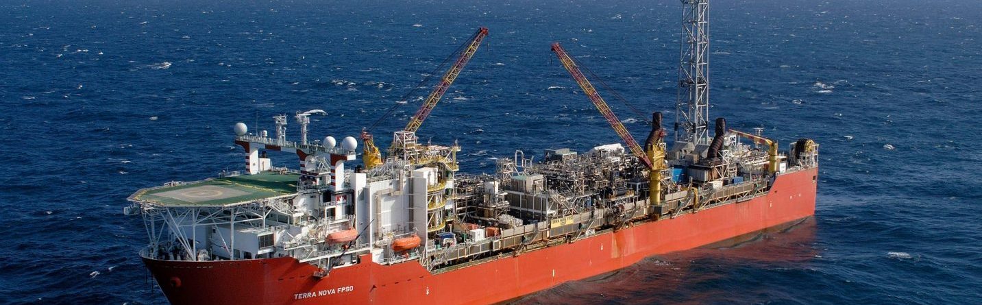A large red floating production storage and offloading (FPSO) vessel sits on the open sea under a partly cloudy sky, equipped with cranes, processing equipment, and a helicopter landing pad.