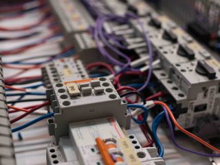 Close-up of an electrical control panel with multiple wires of various colors connected to circuit breakers and relays, showing detailed components and labels.