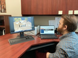 A man sits at a desk with a desktop monitor displaying the word