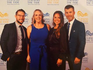 Four people stand smiling together in formal attire in front of a 