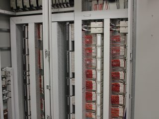 A close-up view of telecommunications or server racks with numerous orange cables and white connection terminals neatly organized inside a gray metal cabinet.