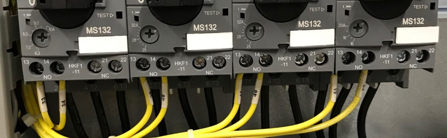 Close-up of an electrical control panel with three ABB MS132 rotary switches, black wires connected above, and yellow wires connected below, mounted on a metal backplate.