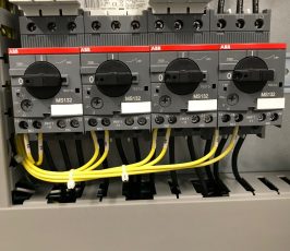 Close-up of an electrical control panel with three ABB MS132 rotary switches, black wires connected above, and yellow wires connected below, mounted on a metal backplate.
