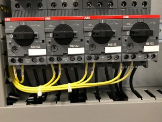 Close-up of an electrical control panel with three ABB MS132 rotary switches, black wires connected above, and yellow wires connected below, mounted on a metal backplate.