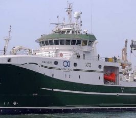 Large green and white research or fishing vessel named "CALVERT," with radar equipment and a Canadian flag, docked in calm water on a clear day.