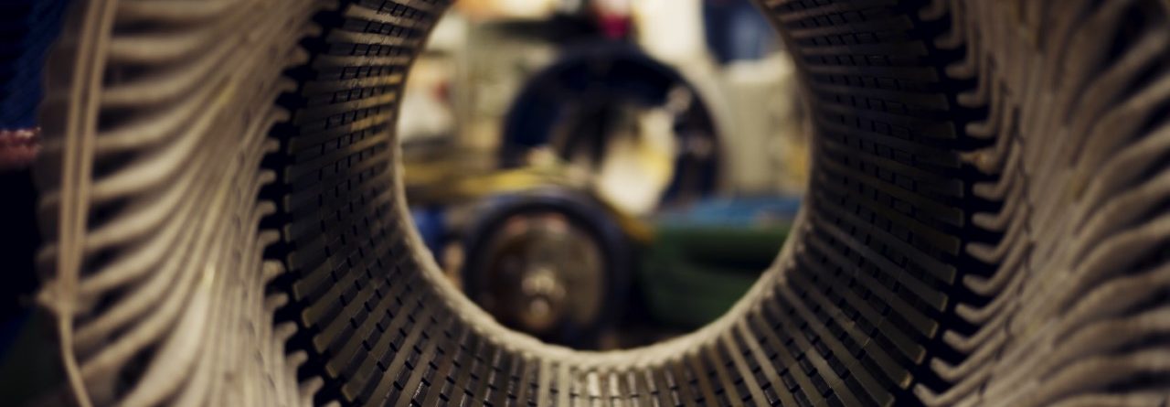 Close-up view through the center of a cylindrical metal structure, likely part of a large electric motor or generator, with visible coils and components in a workshop setting.