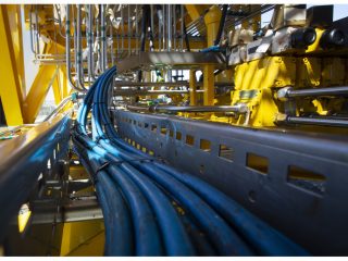 A close-up view of blue industrial cables and metal pipes running through a yellow structure, possibly part of machinery or equipment at an industrial site.
