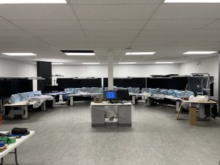 A modern office with curved desks arranged in a semicircle, multiple covered computer monitors, and some unpacked equipment. Two desks with computers are in the center. The room appears to be in the process of being set up.