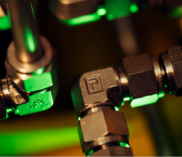 Close-up of metal pipe fittings with a prominent elbow joint marked with the letter "P," illuminated by green and yellow lighting, highlighting industrial machinery components.